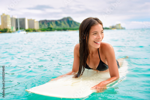 Surfing Asian woman surfer girl on surf lesson in Hawaii paddling on surfboard in ocean. Sexy sports athlete training in water. Watersport active lifestyle.