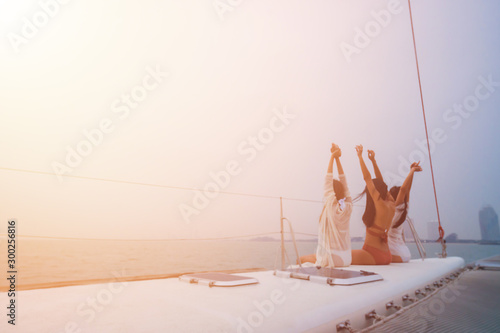 Rear view of three cheerful young women in bikini sitting on boat and admiring sea view