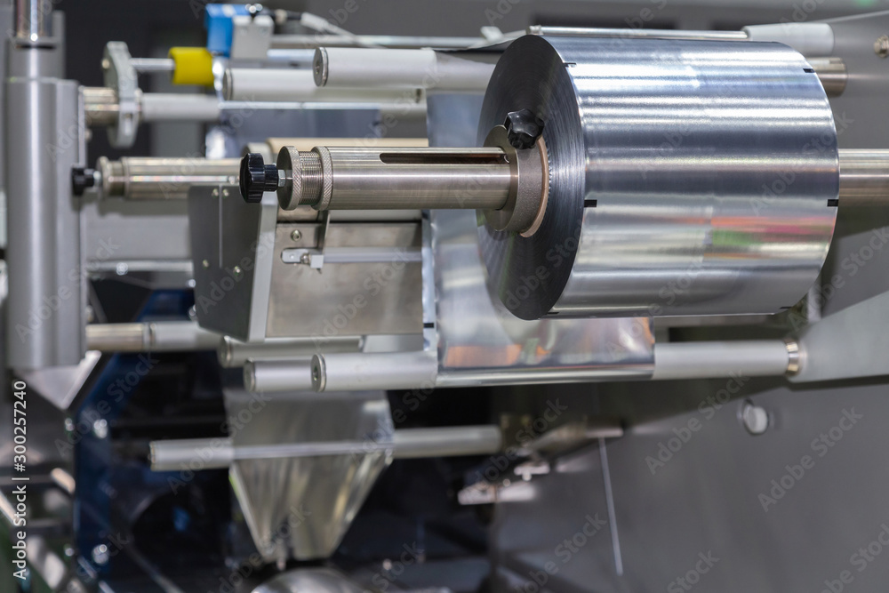 roll of aluminum foil for food packaging on the automatic packing machine in food product factory. industrial and technology concept. roll of aluminum foil for food packaging on the automatic packing machine in food product factory. industrial and technology concept.