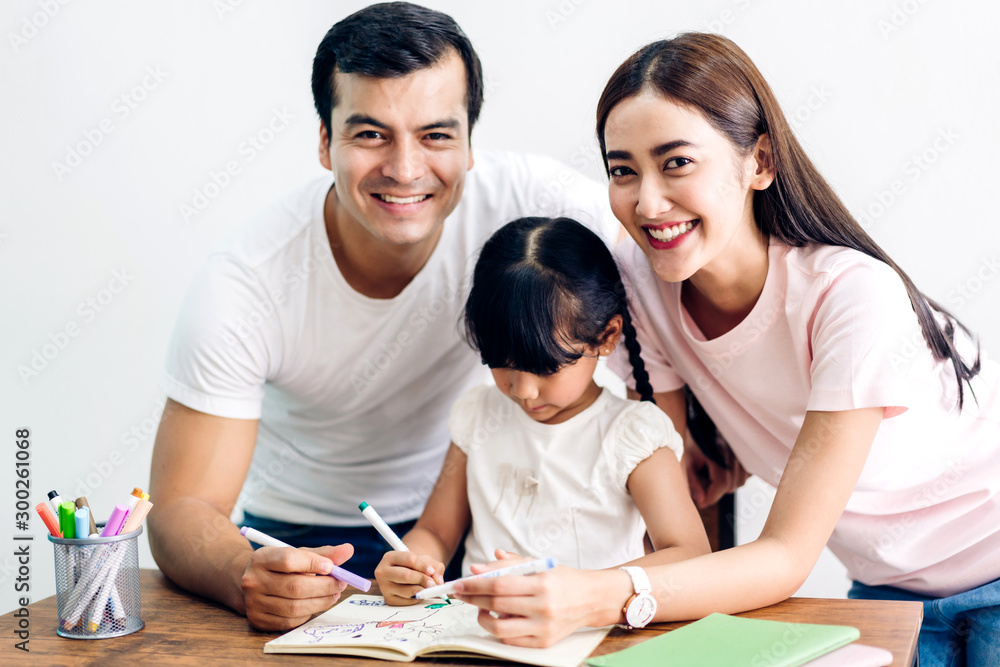 Happy family father and mother with daughter learning and writing in notebook with pencil making homework at home.Education concept Happy family father and mother with daughter learning and writing in notebook with pencil making homework at home.Education concept