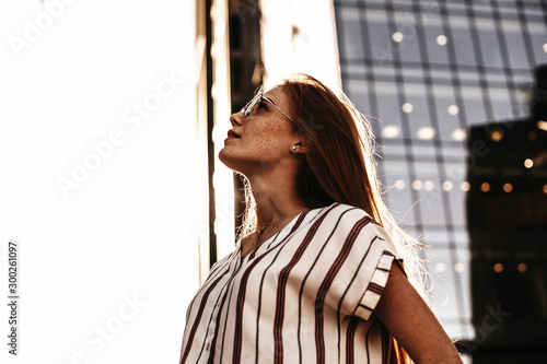 Side view portrait of a lovely red haired woman with freckles looking up seriously against modern business. photo