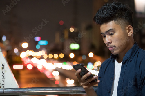 Face of young Asian man using phone against view of the city streets at night
