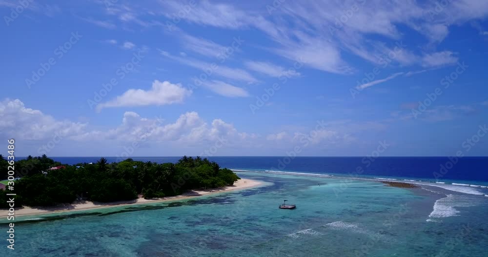 Wide waves interrupted by coral reef barriers keeping lagoon water calm and island's beach untouched in Maldives