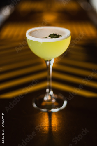 A yellow alcoholic drink in a cocktail nick and nora glass at the bar counter. Selected focus.