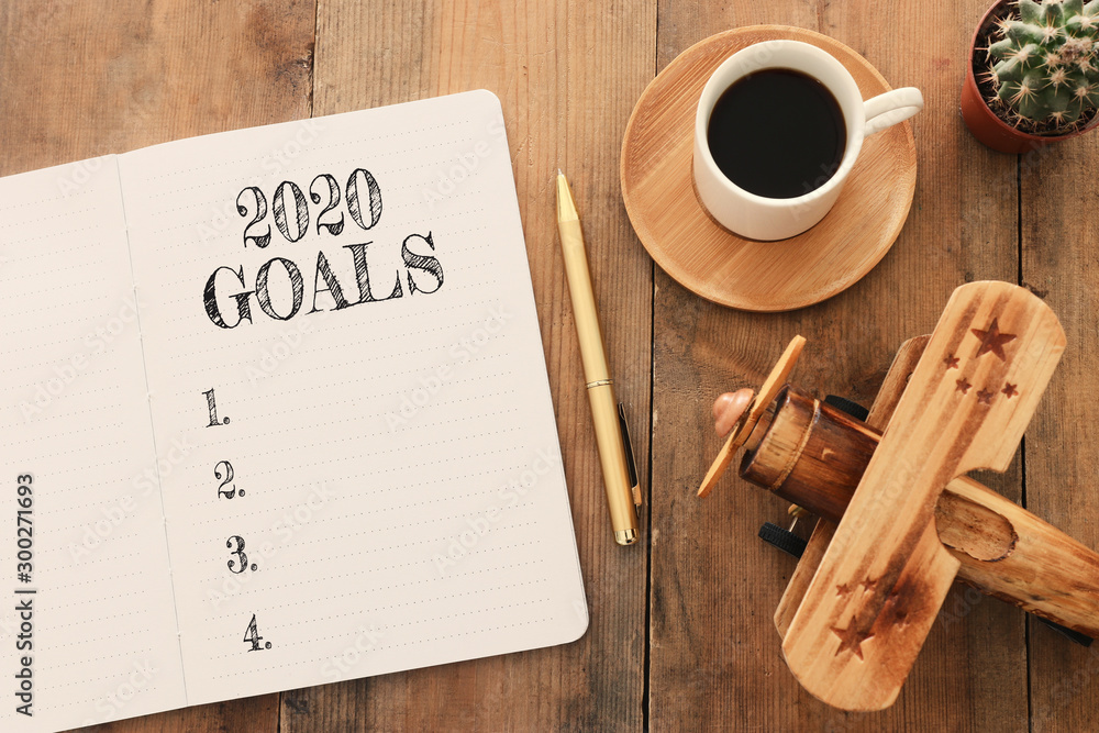 Business concept of top view 2020 goals list with notebook, cup of coffee and old plane toy over wooden desk - obrazy, fototapety, plakaty 