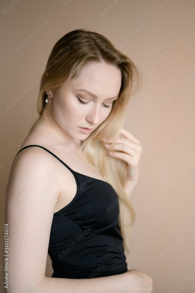 Graceful young woman in a black top posing against beige wall. Graceful young woman in a black top posing against beige wall.