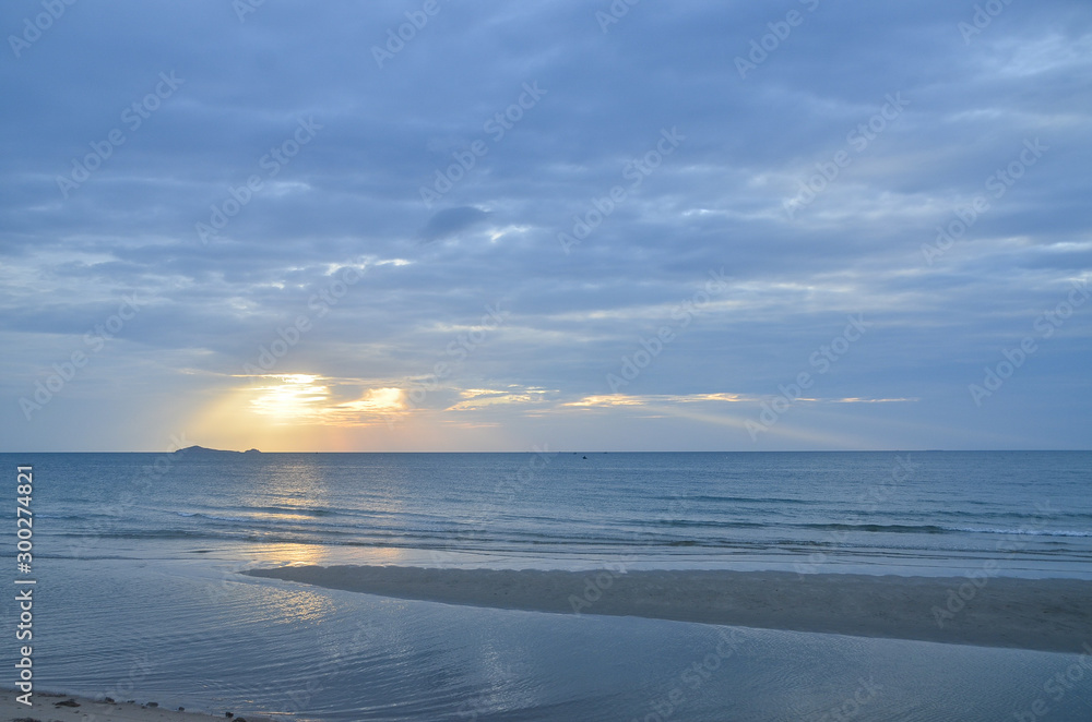 A picturesque tropical yellow coloured cloudy coastal sunrise seascape in a steel blue sky. Thailand.