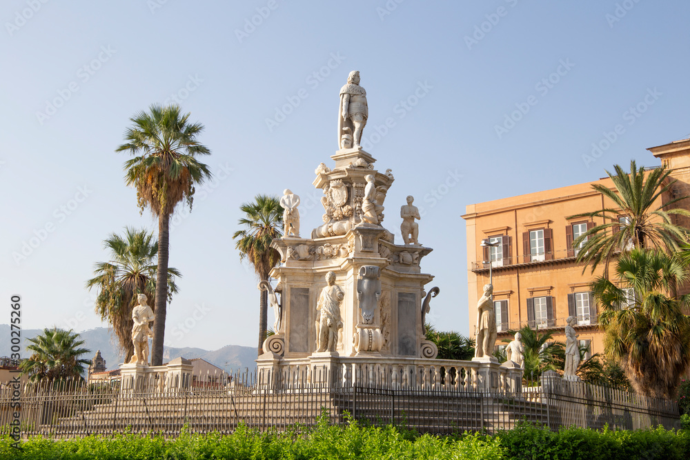 Obraz premium Palermo, Italy, September 19, 2019: A house with a classic statue next door and palm trees outside the street on a sunny day in Palermo. 