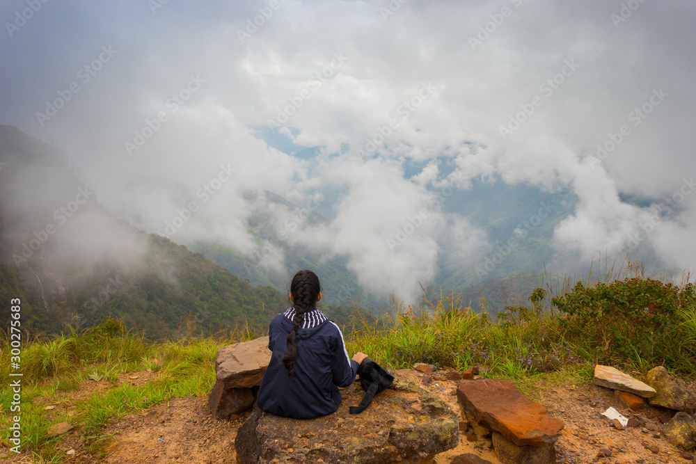 Obraz premium Lost in the clouds. The young girl with braided hair is taking a rest after hiking in the magnificent lush green mountain valley covered with forest and clouds, Shillong, Northeast, Meghalaya, India