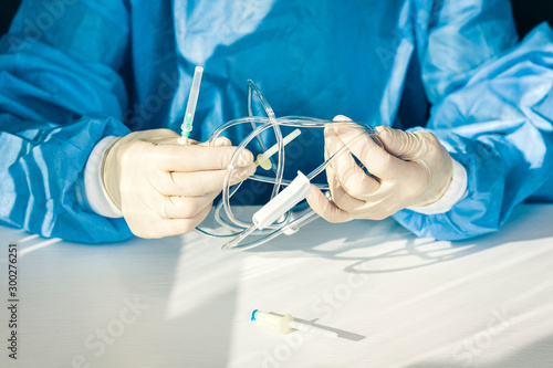 doctor in a blue surgical gown and mask holds in his hand a medical dropper system (medical background with an intravenous IS).
