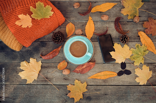 Cup of coffee, autumn leaves and a smartphone on a wooden background. Top view .