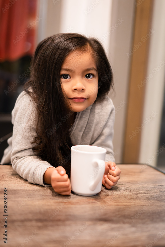 Cute Young Girl Sitting at a Table Drinking Hot Cocoa from a Mug Cute Young Girl Sitting at a Table Drinking Hot Cocoa from a Mug