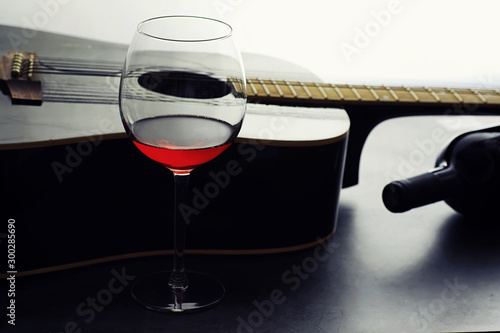Guitar and high glass with red wine on a stone background.
