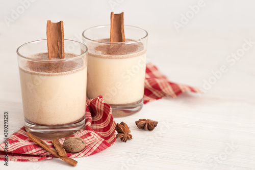 Eggnog in glass cups with a delicate foam, spices and a cinnamon stick photo