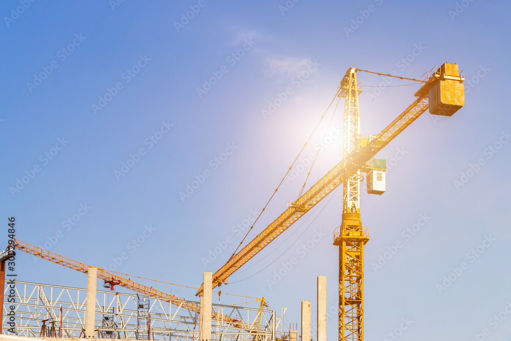 A construction site including several cranes working on a building, Boom crane on the construction of a high-rise and scaffolding in the building,with blue sky background A construction site including several cranes working on a building, Boom crane on the construction of a high-rise and scaffolding in the building,with blue sky background