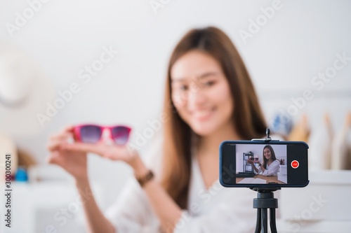 Beautiful asian woman blogger is showing and review product.In front of the smartphone camera to recording vlog video live streaming at home.Business online influencer on social media concept.