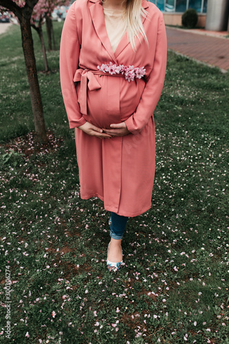 Beautiful pregnant women in pink outfit photographed next to blossom tree in the spring. Close up of her belly. No face shown.