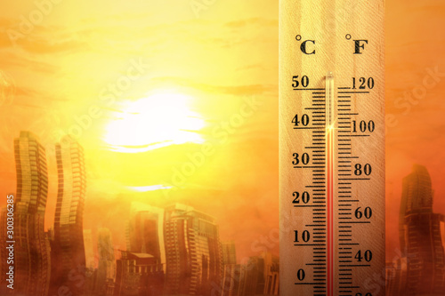 Thermometer with high temperature on the city with glowing sun background