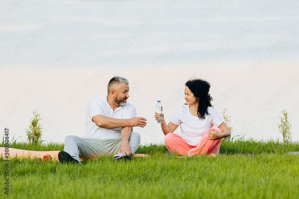 Happy senior woman and man sitting and having a rest. Woman gives a water to man.- Image Happy senior woman and man sitting and having a rest. Woman gives a water to man.- Image