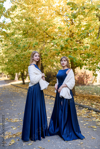 Two very beautiful young ladies in fashionable blue dresses in autumn park.