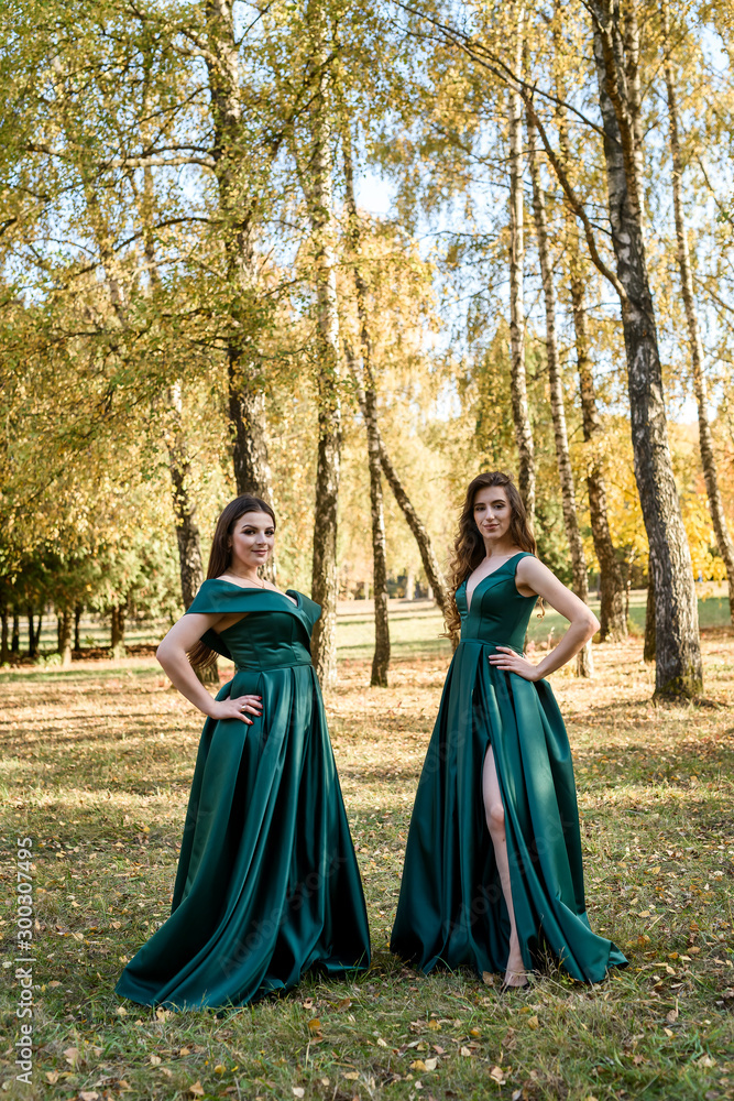 Naklejka premium Ladies in elegant green dresses walking in autumn park. Brunette girl Dreamy young girls laughing on the outdoors