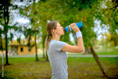Girl athlete is training outdoors. Drinks water and rests after jogging. Healthy lifestyle.