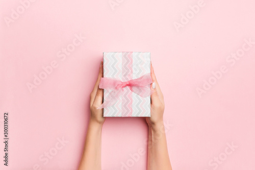 Female's hands holding striped gift box with colored ribbon on living coral background. Christmas concept or other holiday handmade present box, concept top view with copy space © sosiukin