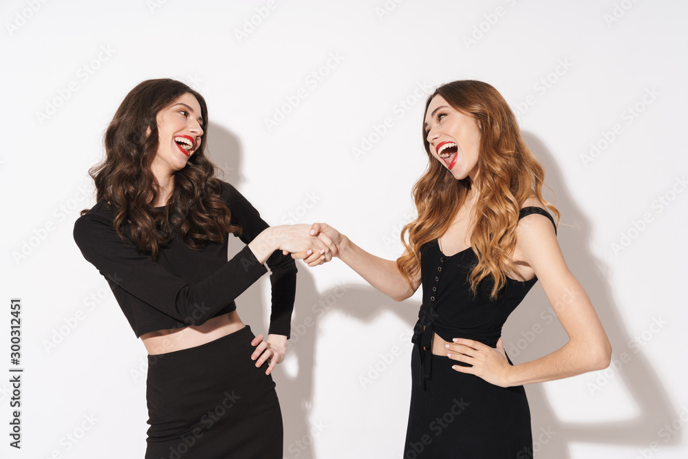 Portrait of two attractive women laughing and shaking hands Portrait of two attractive women laughing and shaking hands