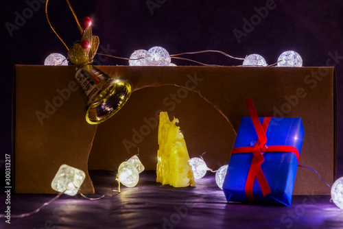 There is rat hole and gold cheese. There are glowing lights inside and on the rat hole. There are blue gift with red ribbon and gold bell near the rat hole. Merry Christmas. Happy New Year 2020.  photo