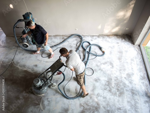 Fototapeta Construction worker in a family home living room that grind the concrete surface before applying epoxy flooring