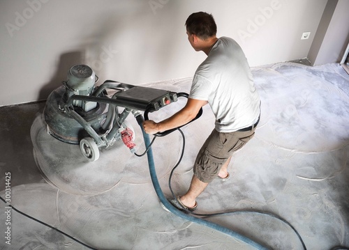 Construction worker in a family home living room that grind the concrete surface before applying epoxy flooring.Polyurethane and epoxy flooring.Concrete grinding. photo