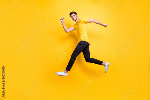Full length photo of handsome guy jumping high speed running competition participant rushing shopping wear casual t-shirt black trousers isolated yellow color background