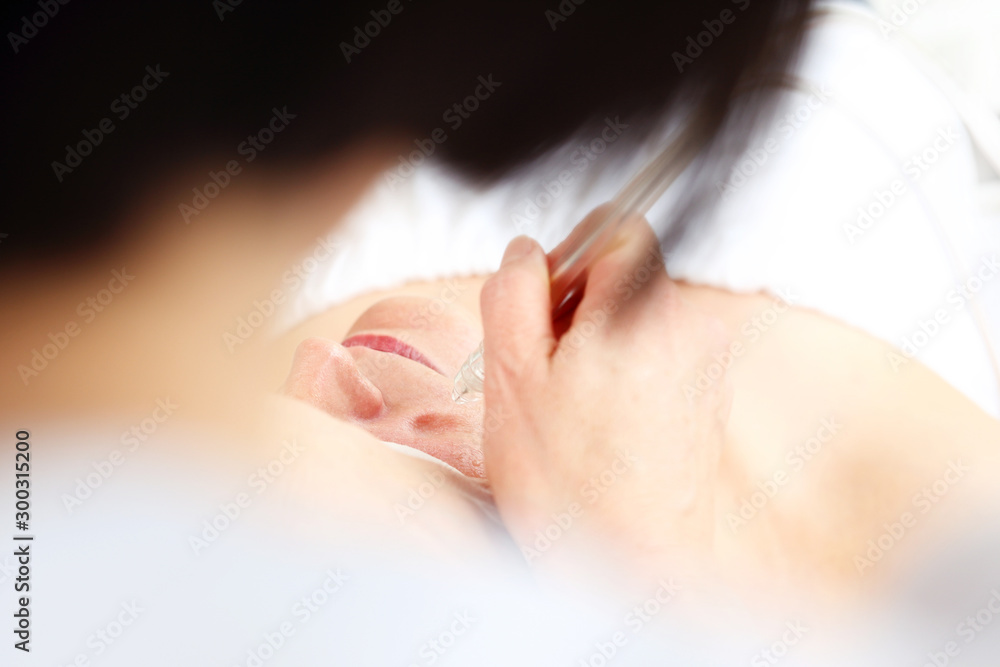 Naklejka premium Oxybrasion treatment, water peeling. The beautician performs oxygen oxybrasion treatment on the skin of a woman's face. Care treatment, skin cleansing
