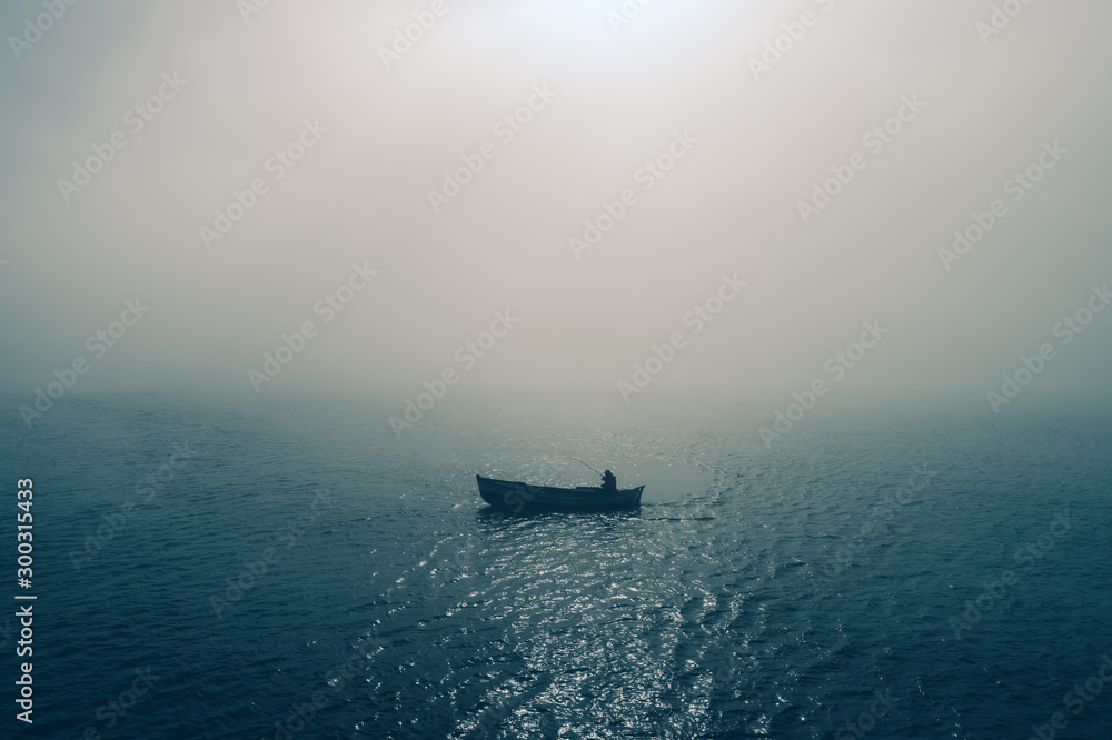 Fishing boat and fisherman in the sea, foggy morning over the water