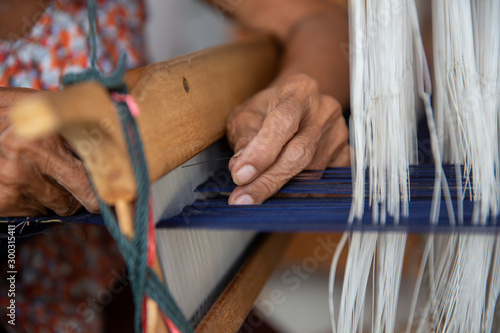 Cotton weaving. Close-up woman hand weaving cotton on manual loom. Thai cotton handmade. Homespun fabric process. The process of fabric weaving in vintage weaver machine. Selective focus.