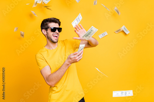 Photo of young handsome careless guy throwing money banknotes away wealthy person wear sun specs casual t-shirt isolated bright yellow color background photo