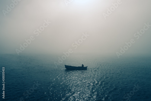 Fishing boat and fisherman in the sea, foggy morning over the water © ValentinValkov