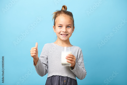Cuadro en lienzo Cheerful child girl drinks milk and shows thumbs up.