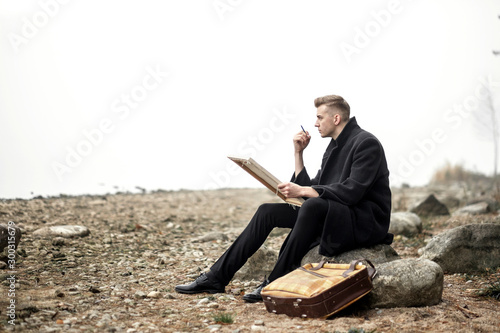 outdoor artist, young man is painting in nature, fashion model in coat