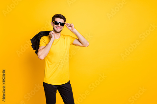 Photo of handsome guy holding boutique bags making abroad shopping self-confident classy person wear casual t-shirt pants isolated yellow color background