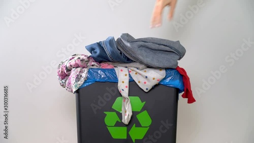 Distribution of waste for recycling at home. A woman's hand puts old clothes in a bin with a sign of recycling photo
