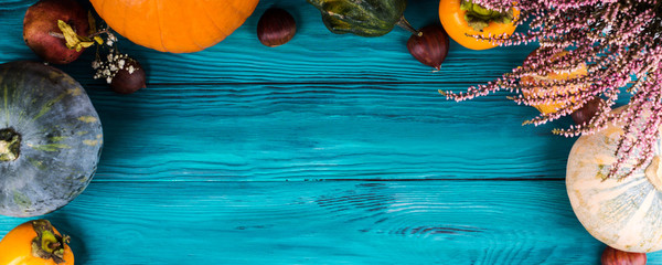Autumn thanksgiving moody background with different pumpkins, fall fruit and flowers on rustic wooden table. Flat lay