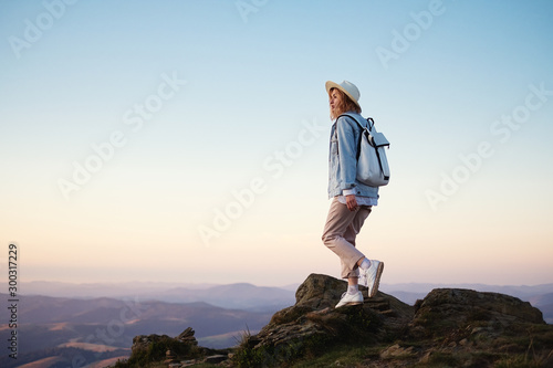 Hiker with a backpack in the mountains. Young girl walking in the mountains during sunset. Mountains and people. Adventure and travel - image
