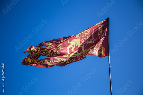Red flag of Venice with golden lion with sword waving in the air on a blue sky