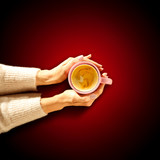 Top view of woman hands with hot drink. Free space for your decoration. Cup of hot chocolate or coffee. Red background of table top. Christmas time. Copy space, aerial view.Dark mood light with shadow