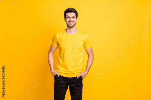 Photo of cheerful attractive man holding hands in pockets of his black pants smiling toothily with bristle isolated over vibrant color background