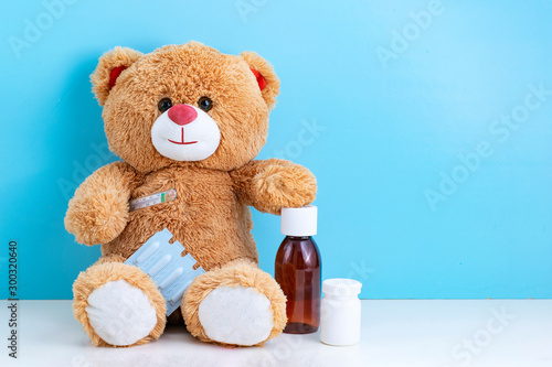 Teddy bear, thermometer, antipyretic candles, pills and cough syrup on blue background with space to copy; concept cheerful Pediatrics; children's medicine