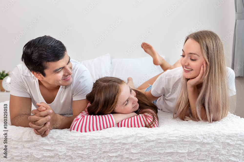 Happy family, including father mother and daughter, are lying down on bed with smile, looking at each other Happy family, including father mother and daughter, are lying down on bed with smile, looking at each other