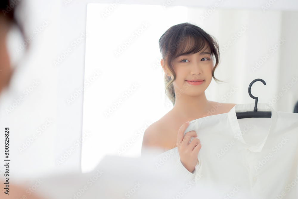 Beautiful asian woman smiling with clothes trying on dress up fitting with modern and looking reflection mirror in the room, girl choose clothes fashion with happy and cheerful, lifestyle concept. Beautiful asian woman smiling with clothes trying on dress up fitting with modern and looking reflection mirror in the room, girl choose clothes fashion with happy and cheerful, lifestyle concept.