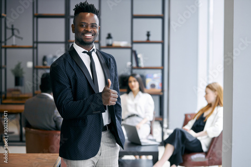 Confident business male wearing formal tuxedo stand posing in office environment and look at camera. thumbs up gesturing. Business people concept